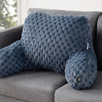 A textured, contoured lumbar pillow in a slate blue color, resting on a gray fabric sofa. The pillow features a raised, bumpy circular pattern and a small power button on the head.