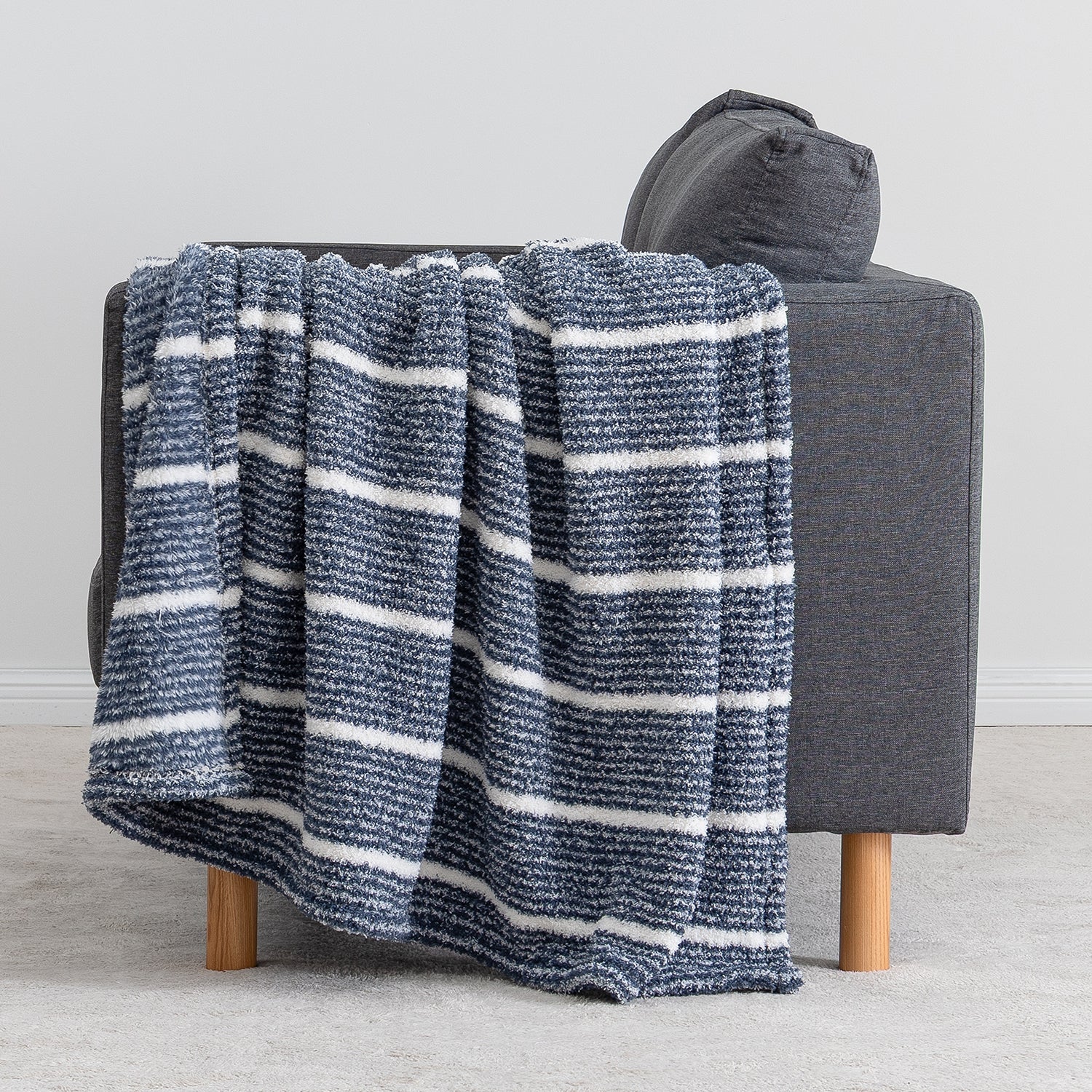 A textured throw blanket with horizontal navy and white stripes draped over a dark gray armchair with light wood legs, set against a neutral gray background.