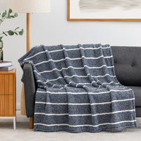 A textured knit throw blanket with horizontal navy and off-white stripes draped over a dark gray sofa in a modern living room setting.