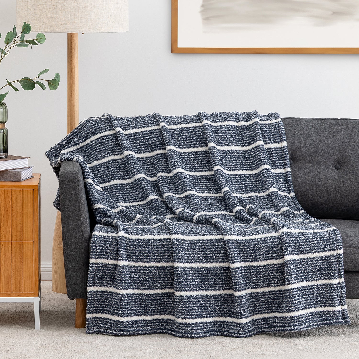 A textured knit throw blanket with horizontal navy and off-white stripes draped over a dark gray sofa in a modern living room setting.