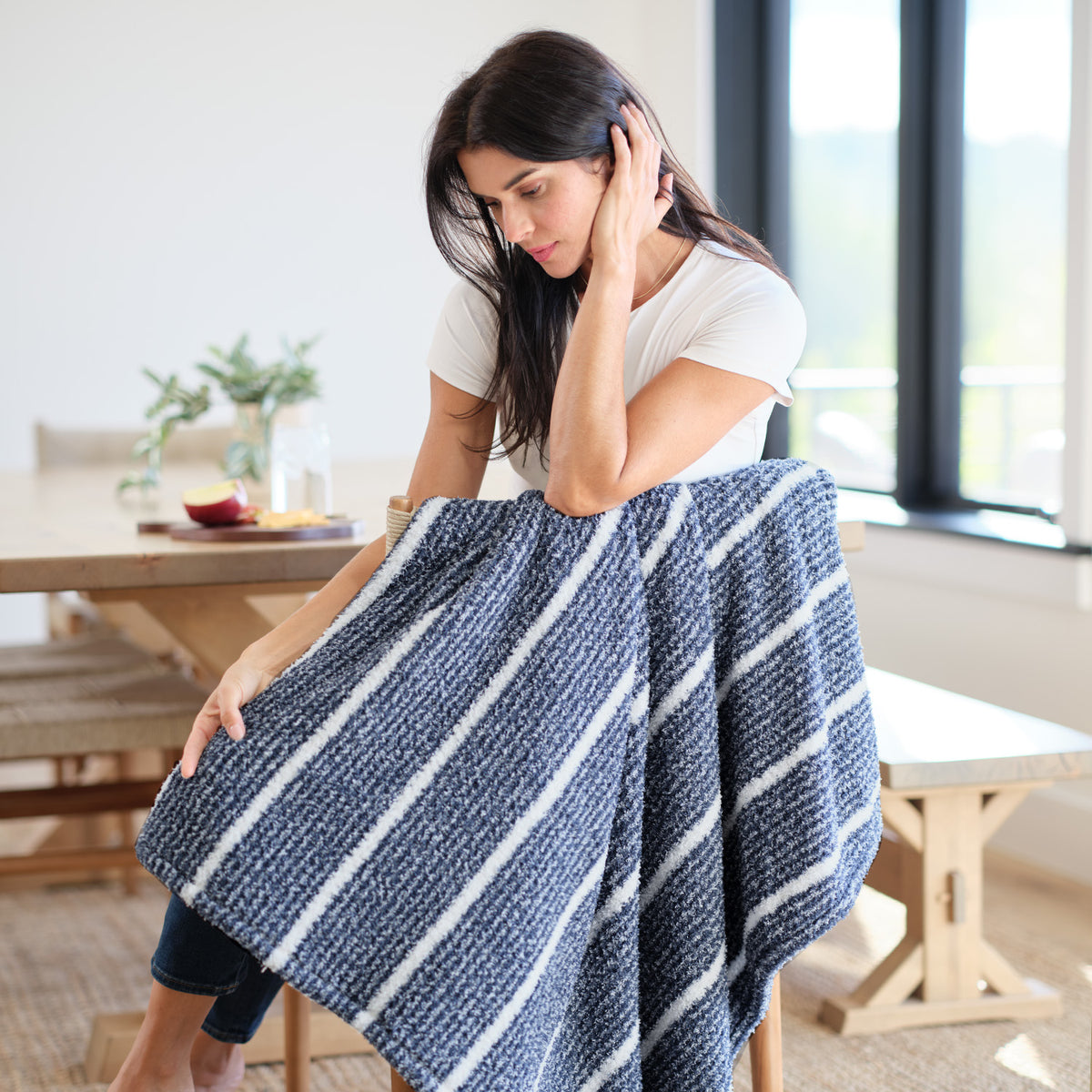 A woman sitting on a wooden chair with a blue striped retro plush throw.