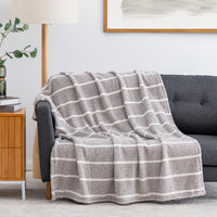 A textured knit throw blanket with horizontal gray and white stripes is draped over a dark gray sofa in a modern living room setting.