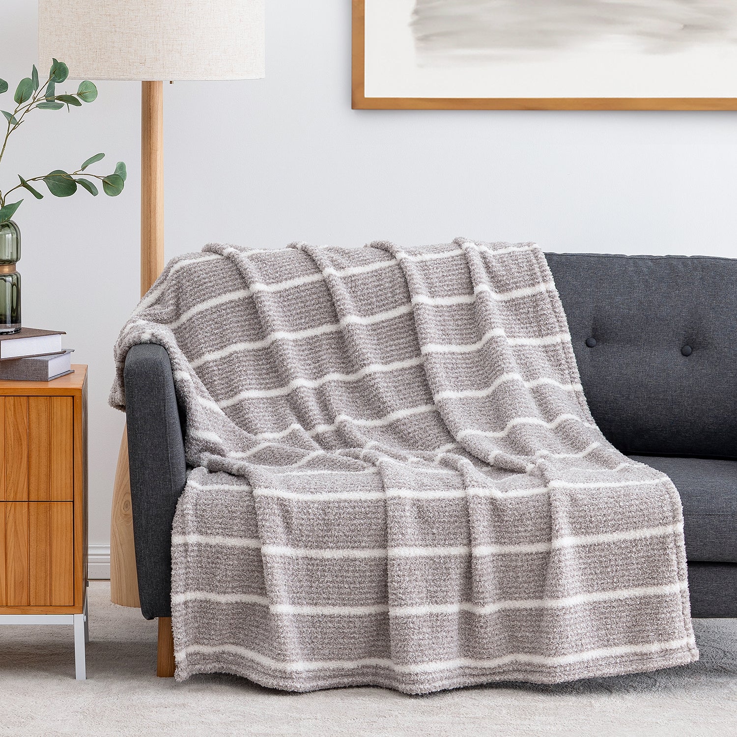 A textured knit throw blanket with horizontal gray and white stripes is draped over a dark gray sofa in a modern living room setting.