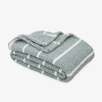 A folded textured throw blanket with white stripes on a light gray background.