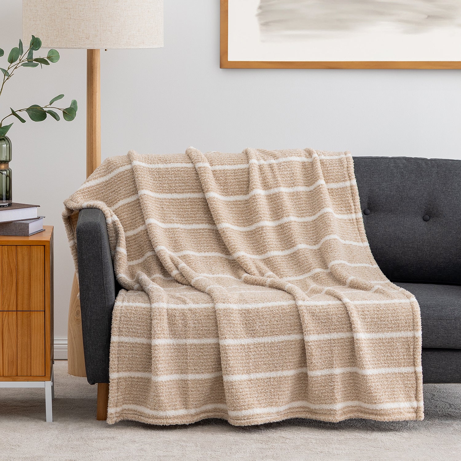 A beige and off-white striped textured throw blanket is draped over a dark gray sofa in a modern living room setting.