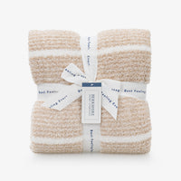 A pair of folded textured knit blankets in beige and white stripes, wrapped together with a white ribbon and tag from Berkshire Hotel Company.