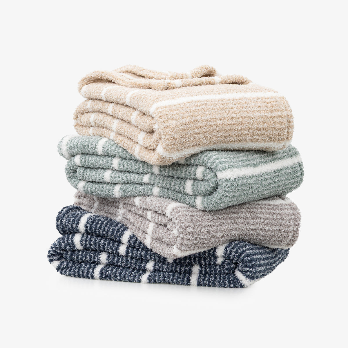 A stack of four folded textured blankets in neutral and muted colors, including beige, sage green, light gray, and navy blue, with white stripes, on a light gray background.