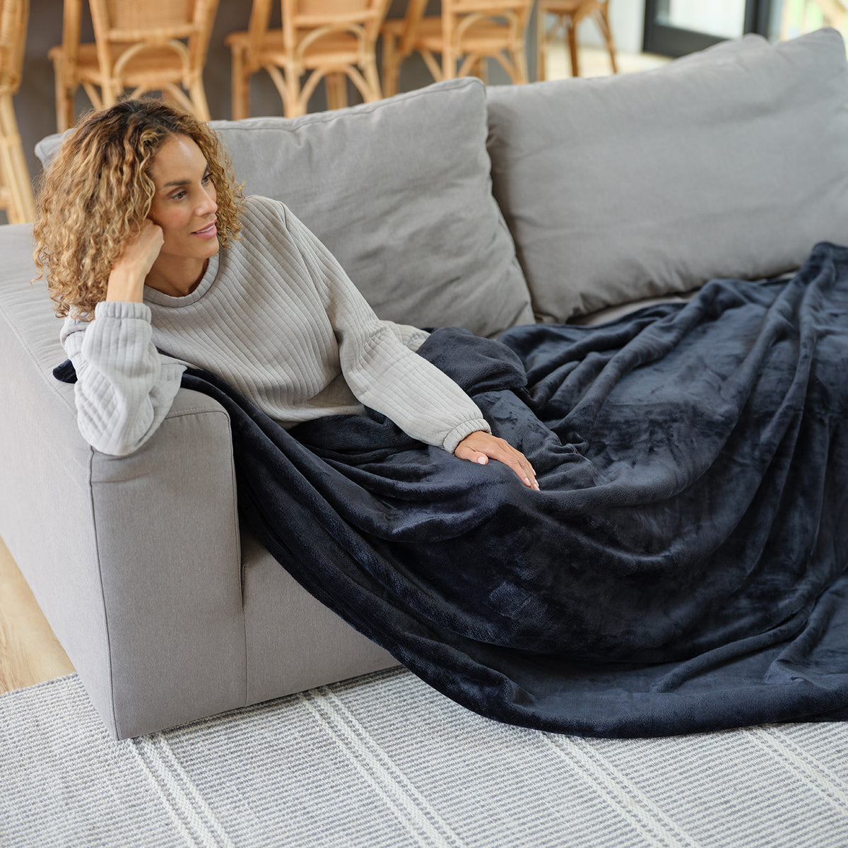 A woman lounging on a grey solfa with a black throw blanket draped over her legs.