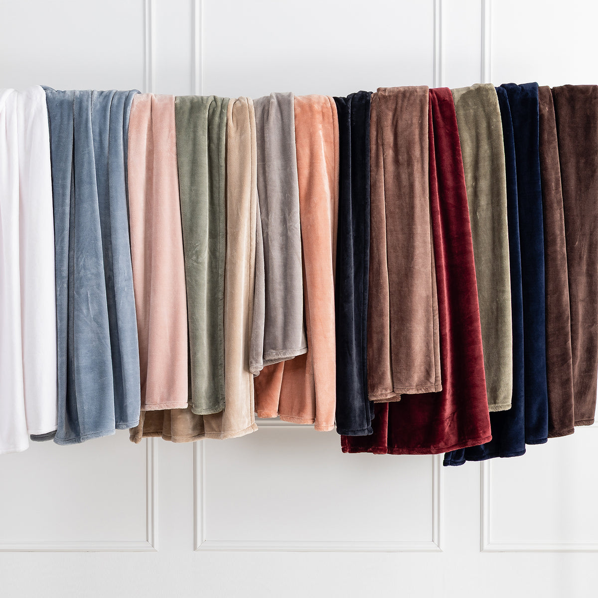 Premium VelvetLoft® Throws in assorted Colors hanging side by side on a rail against a white paneled wall