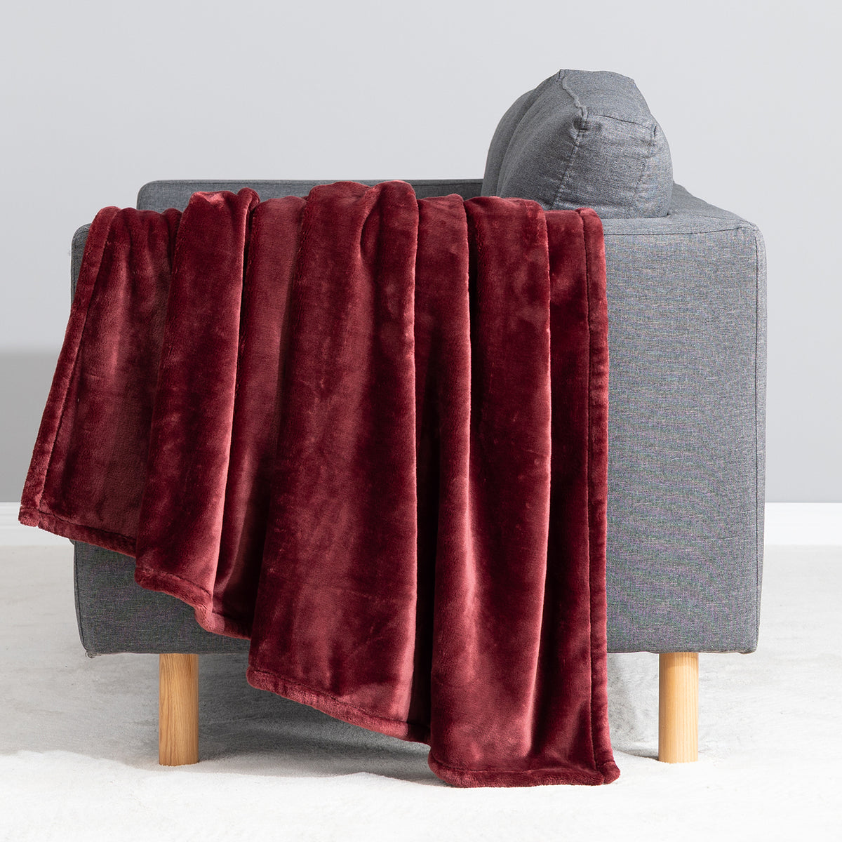 Premium VelvetLoft® Throw in Roanoke Red, draped over the arm of a gray sofa, close view