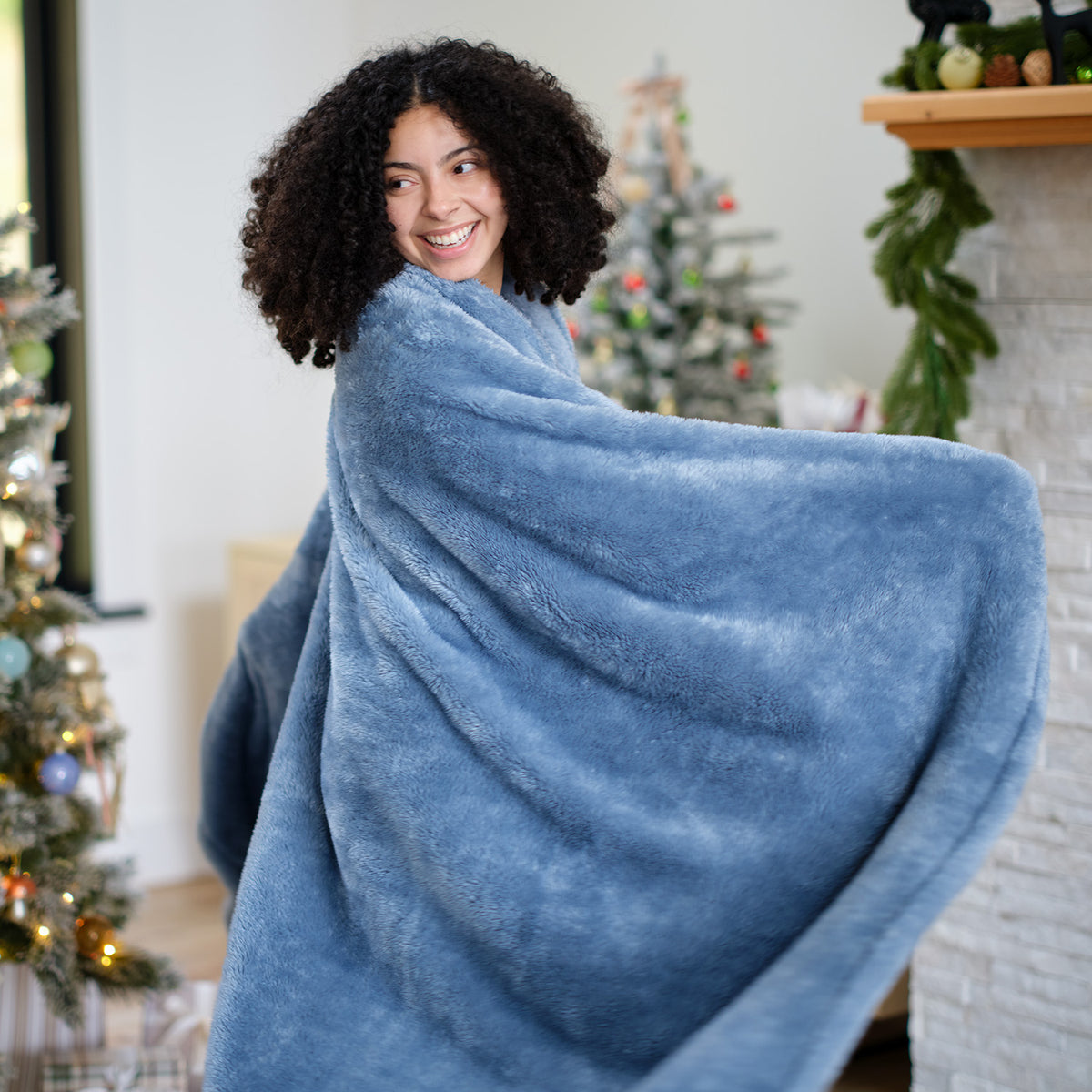 A woman standing in a holiday decorated room with a blue Premium Extra-Fluffy Throw.