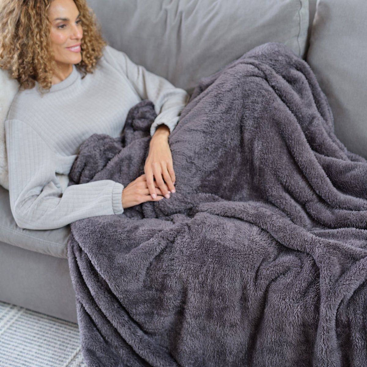 A woman laying on a grey sofa with a grey Premium Extra-Fluffy Throw.