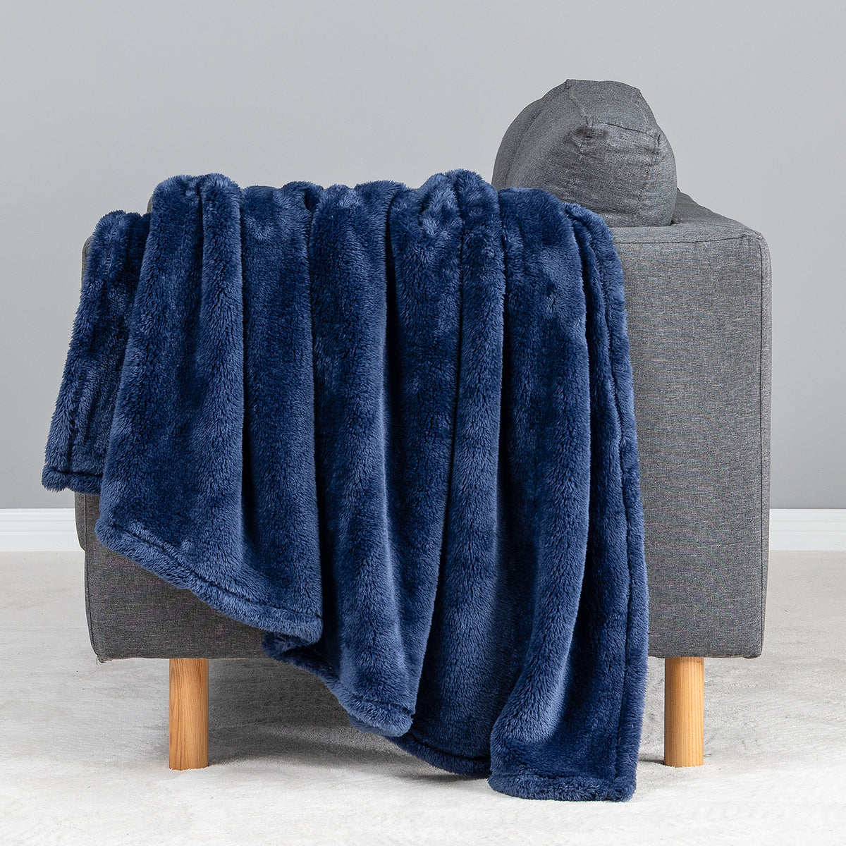 Premium Extra-Fluffy™ Throw in Dress Blue draped over the arm of a gray sofa, close view