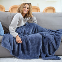 A woman sitting on a grey sofa with a blue Premium Extra-Fluffy Throw.
