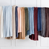 Premium Extra-Fluffy™ Throws in assorted Colors hanging side by side on a rail against a white paneled wall