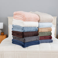 Folded Premium Extra-Fluffy™ Throws in assorted Colors stacked on a bed