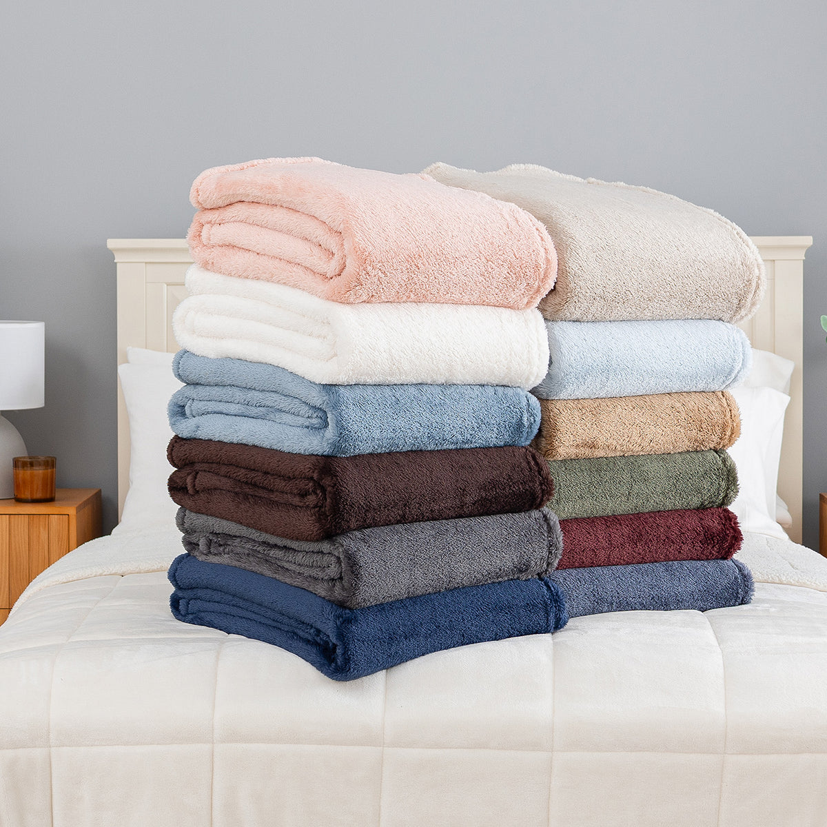 Folded Premium Extra-Fluffy™ Throws in assorted Colors stacked on a bed