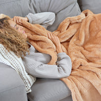 A woman laying on a grey sofa with an orange toned Premium Extra-Fluffy Throw.
