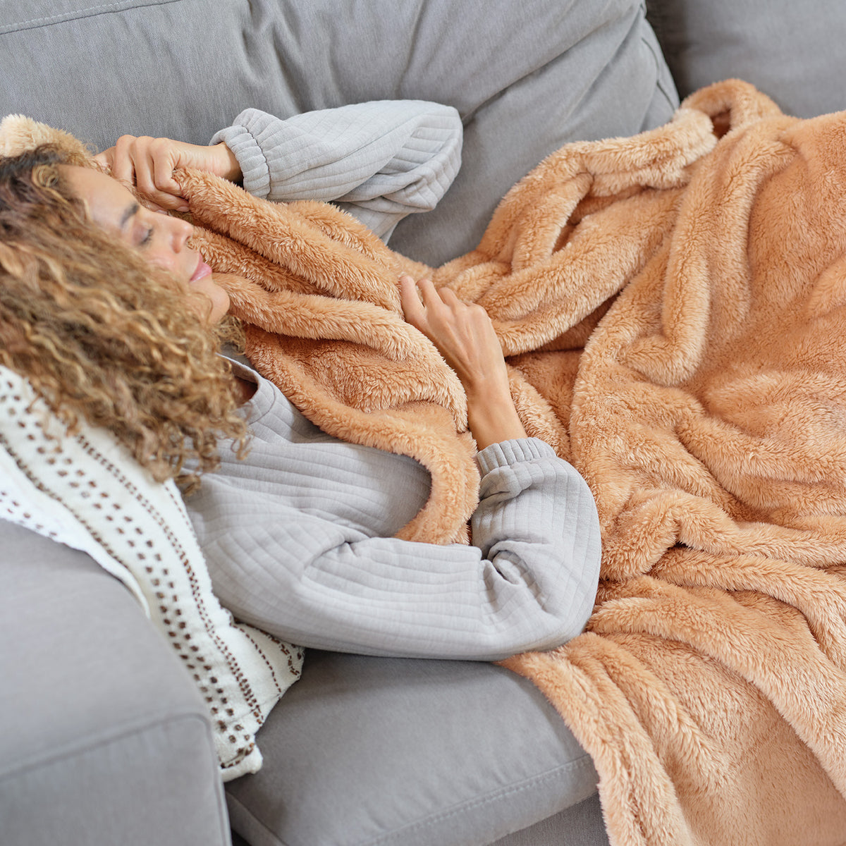 A woman laying on a grey sofa with an orange toned Premium Extra-Fluffy Throw.