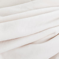 A close-up of soft, draped fabric in a very light warm off-white or blush tone, showing the texture and folds of the material.