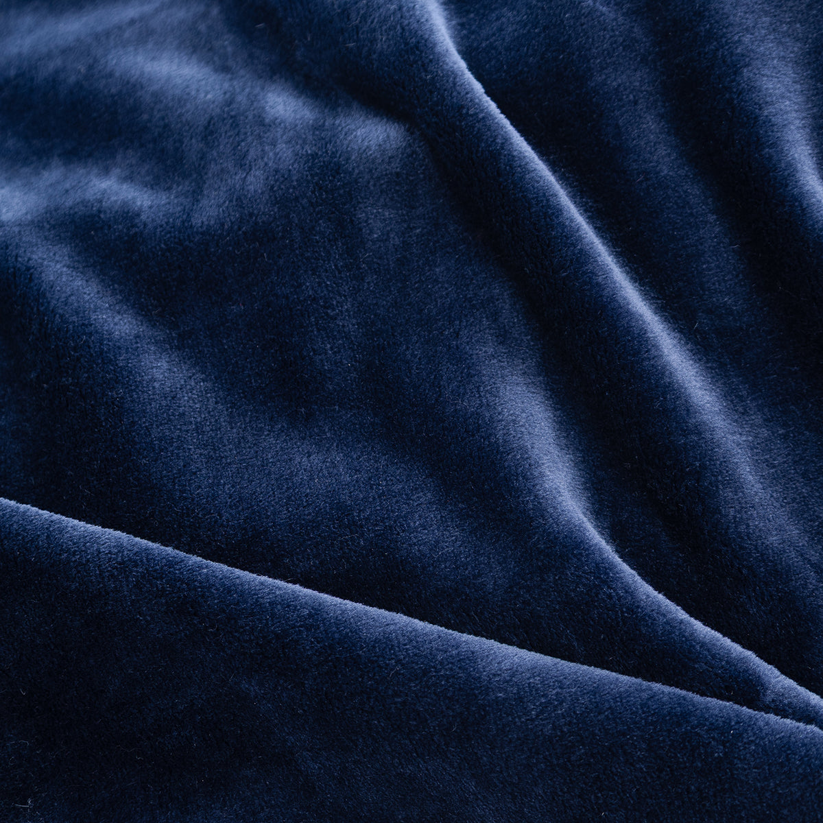 A close-up of draped navy blue velvet fabric, showing its soft texture and rich color with gentle folds.
