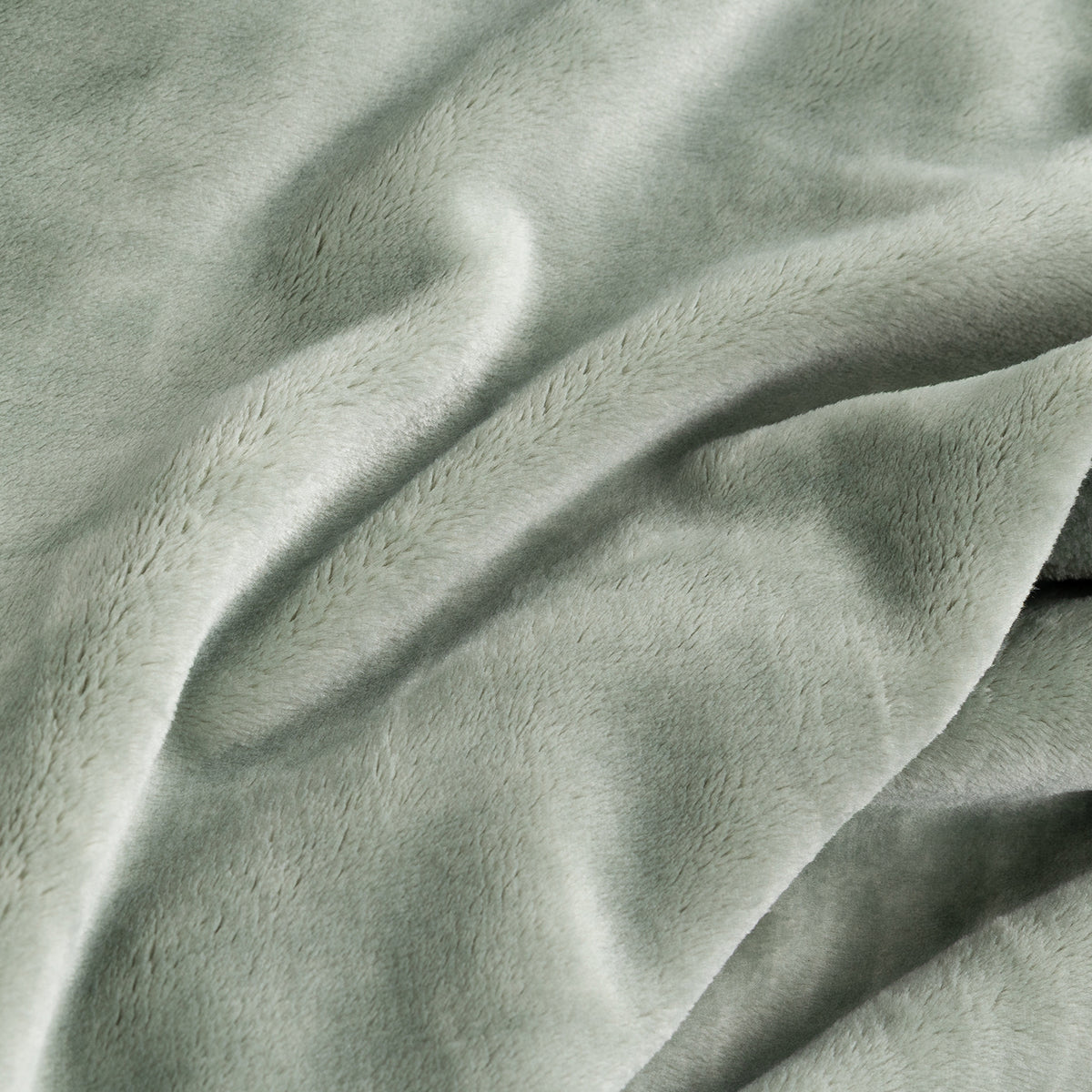 A close-up of soft, plush fabric in a muted sage green color, showing the texture and folds of the material.