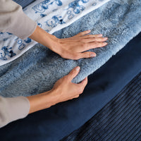 A person touching a blue Premium Extra-Fluffy Blanket layered on a bed.