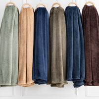 Premium Extra-Fluffy™ Blankets in six deeper Colors hanging side by side on a rail against a white paneled wall