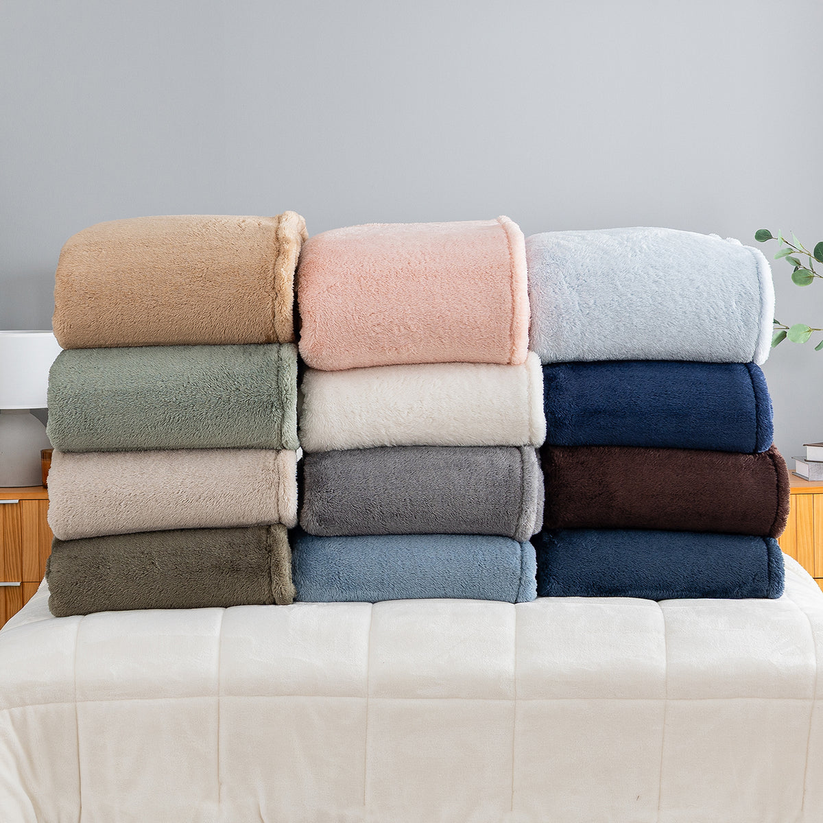 Folded Premium Extra-Fluffy™ Blankets in twelve Colors stacked on a bed