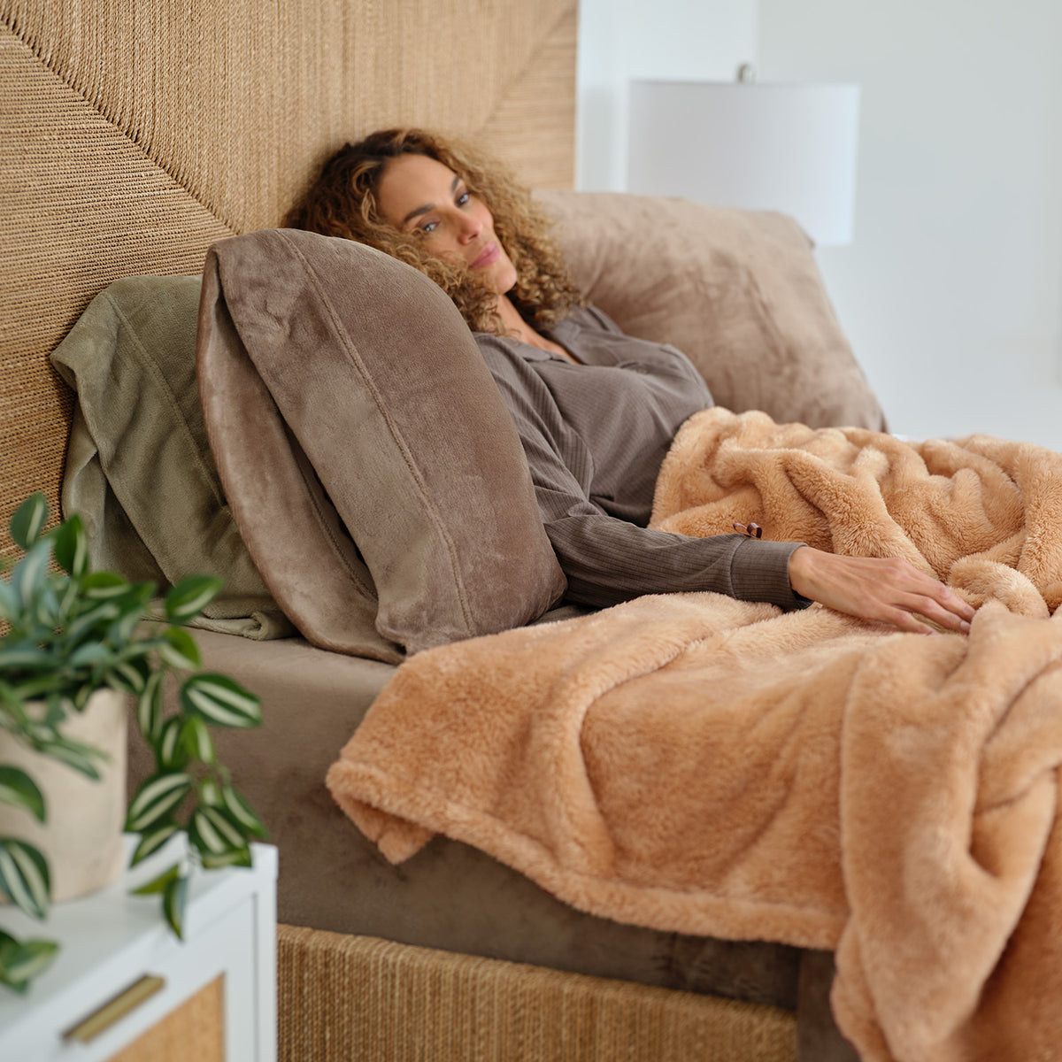 A woman laying in a cozy warm bed with a tan Premium Extra-Fluffy Blanket.