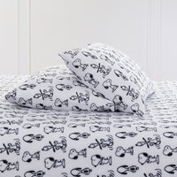 Close up of two pillows and a bed dressed with Peanuts printed VelvetLoft Sheets.