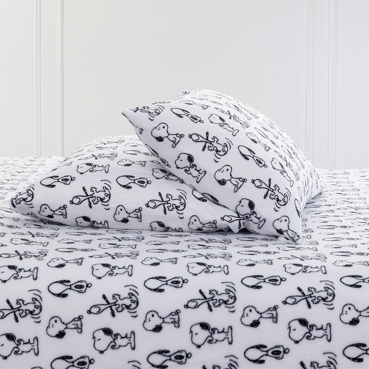 Close up of two pillows and a bed dressed with Peanuts printed VelvetLoft Sheets.