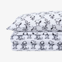 A folded stack of white fabric sheets, printed with a black cartoon character pattern resembling Snoopy and Woodstock.