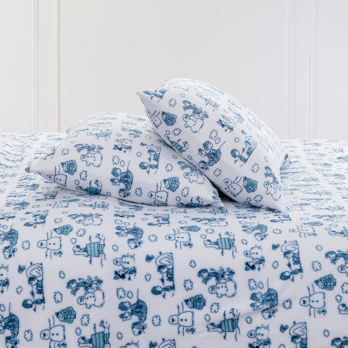 A bed made up with a white bedding set featuring a blue hand-drawn cartoon animal and cloud pattern, including two matching pillows and a comforter.