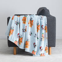 A blue gingerbread holiday Peanuts Printed VelvetLoft Throw draped neatly over a grey chair.