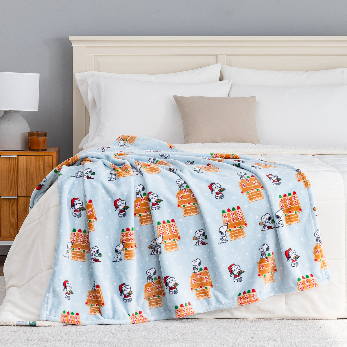 A blue gingerbread holiday Peanuts Printed VelvetLoft Throw draped neatly over a bed.