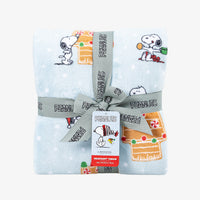 A holiday Peanuts Printed VelvetLoft Throw folded neatly with a ribbon on a white surface.