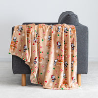 A gingerbread holiday Peanuts Printed VelvetLoft Throw draped over a grey chair.