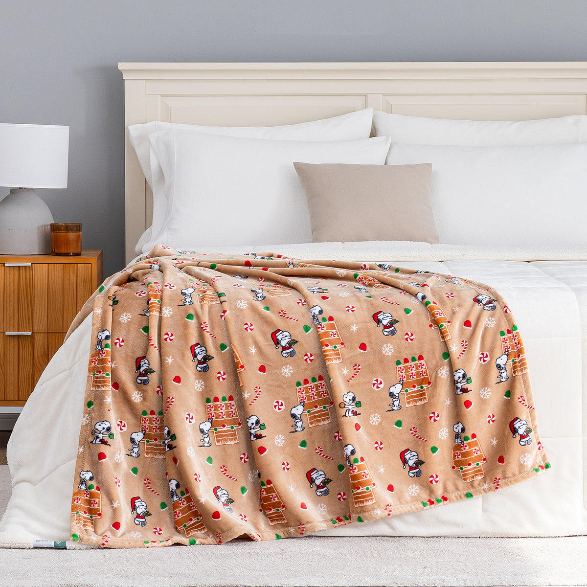 A gingerbread holiday Peanuts Printed VelvetLoft Throw draped neatly over a bed.
