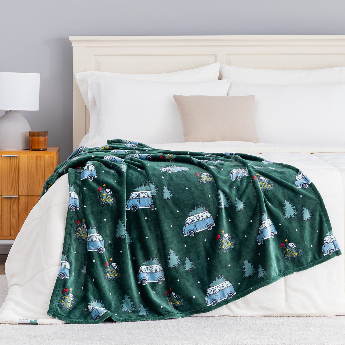 A green holiday Peanuts Printed VelvetLoft Throw draped neatly over a bed.