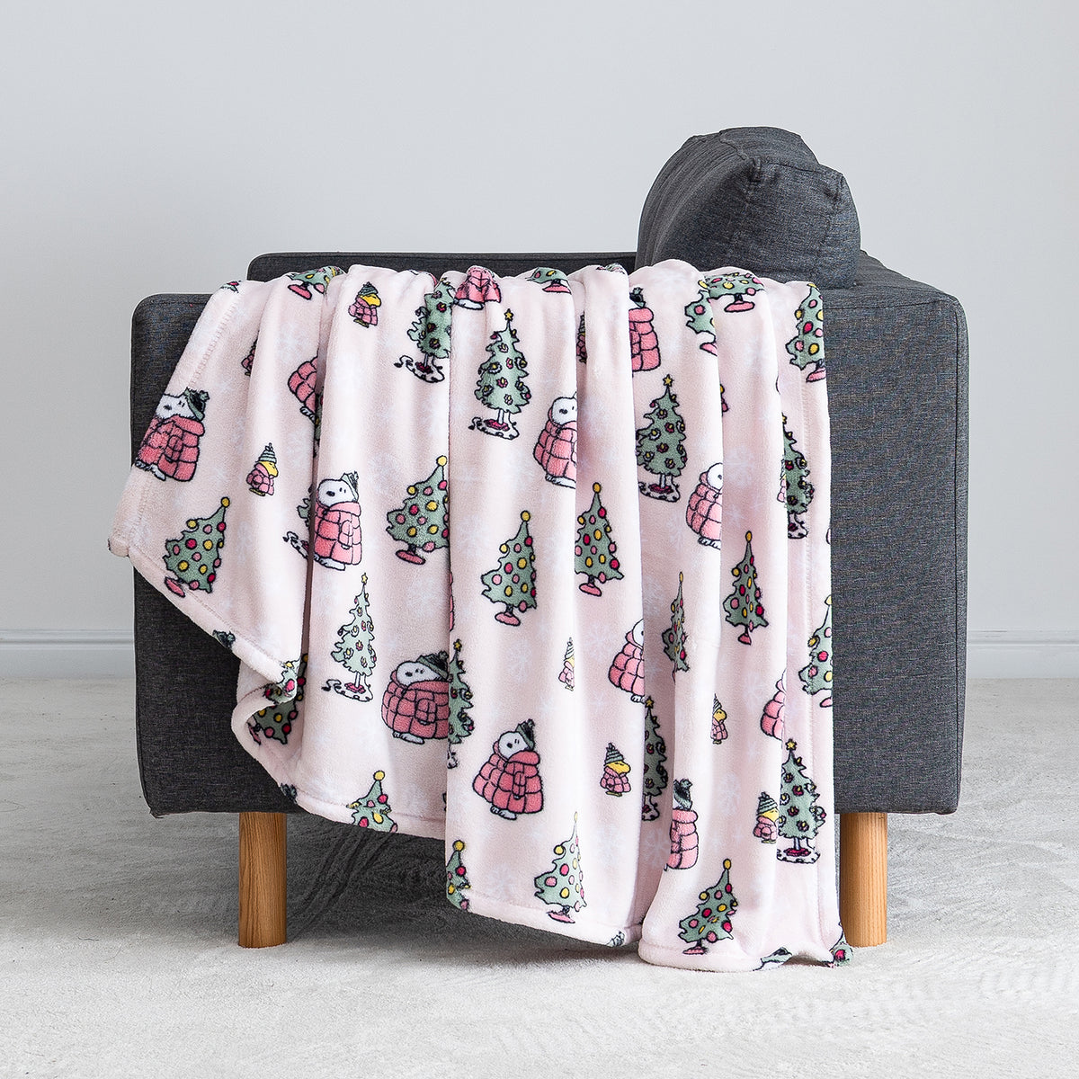 A pink holiday Peanuts Printed VelvetLoft Throw draped over a grey chair.