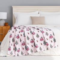 A pink holiday Peanuts Printed VelvetLoft Throw draped neatly over a bed.