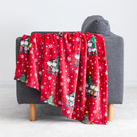 A red holiday Peanuts Printed VelvetLoft Throw draped over a red chair.