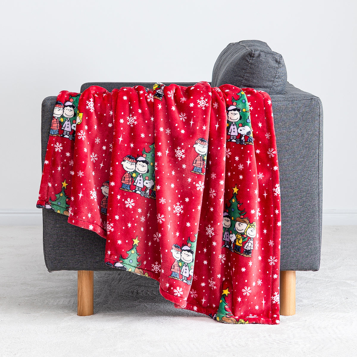 A red holiday Peanuts Printed VelvetLoft Throw draped over a red chair.