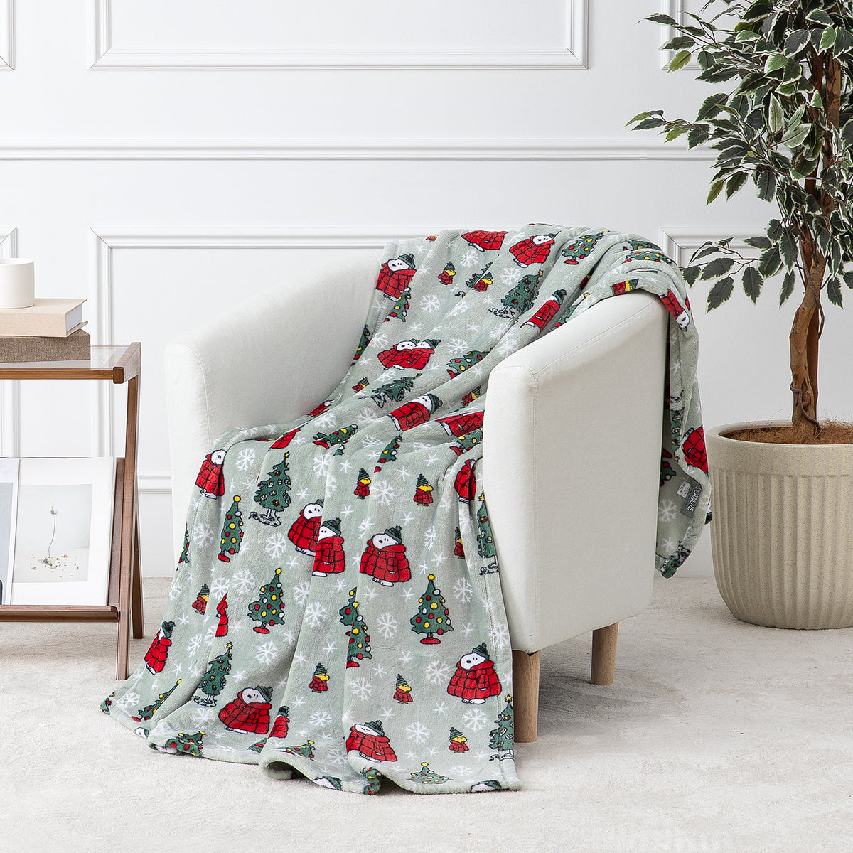 A sage green holiday Peanuts Printed VelvetLoft Throw draped over a white chair.