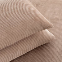 Close-up of two ribbed corduroy pillows in a warm taupe-beige color, stacked diagonally on a matching corduroy surface.