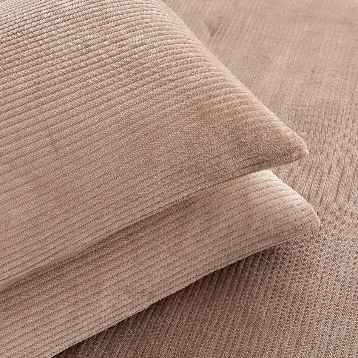 Close-up of two ribbed corduroy pillows in a warm taupe-beige color, stacked diagonally on a matching corduroy surface.