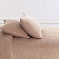 Two beige ribbed throw pillows resting on a matching beige ribbed comforter in a softly lit interior with white wall molding.