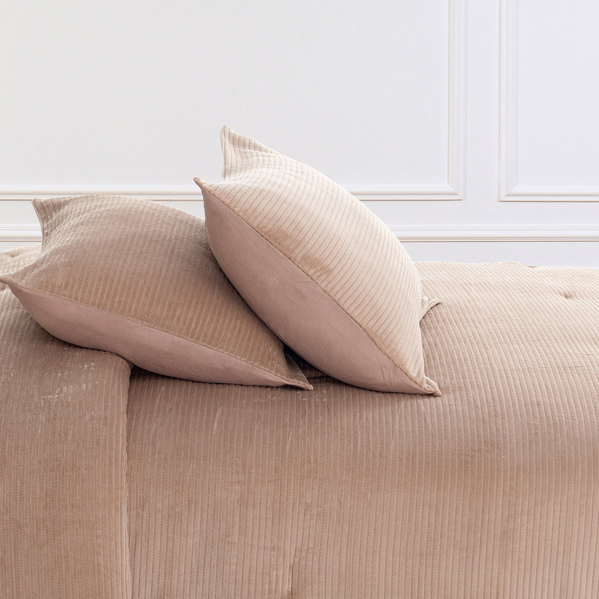 Two beige ribbed throw pillows resting on a matching beige ribbed comforter in a softly lit interior with white wall molding.