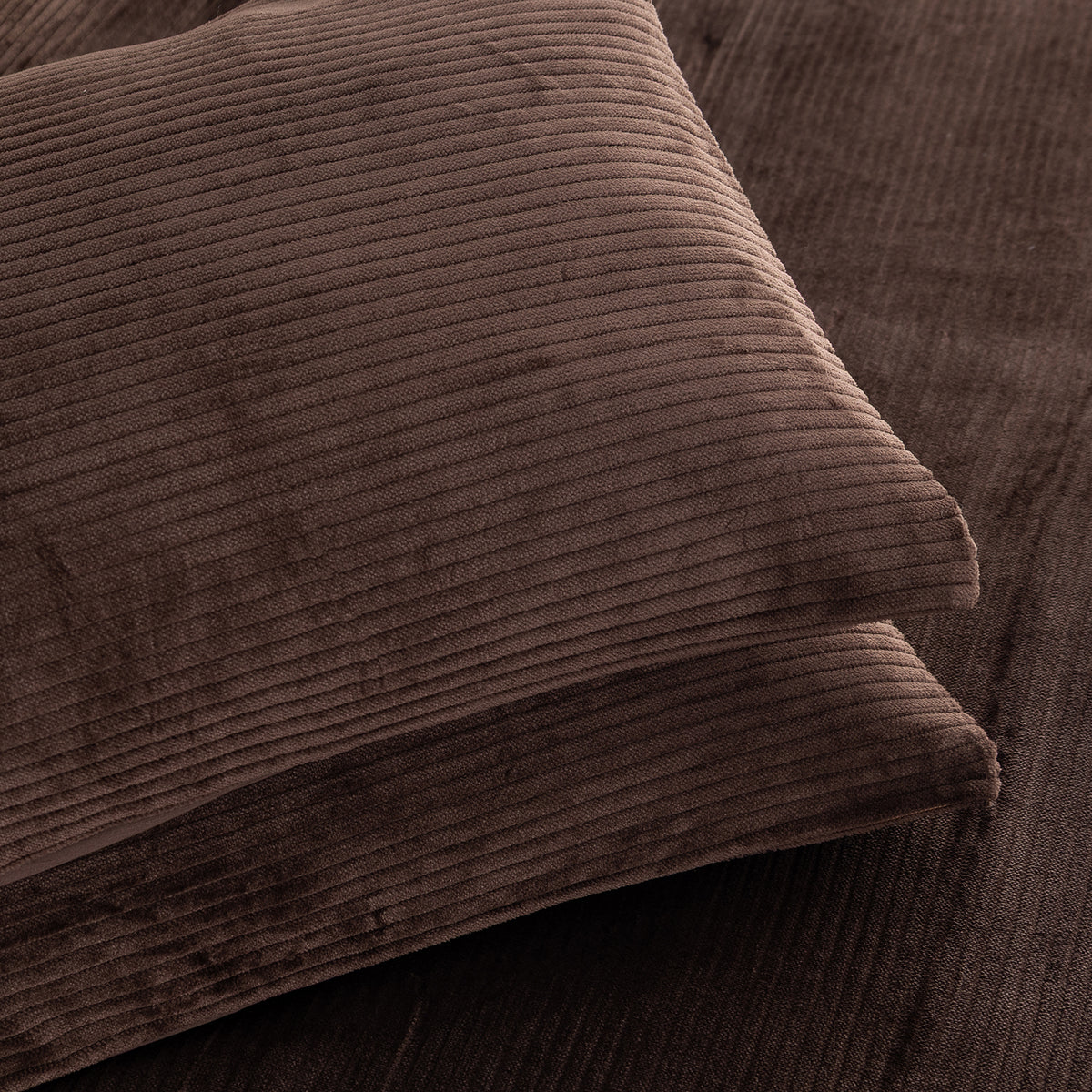 A close-up of two brown corduroy pillows stacked on a matching brown corduroy surface, showing the ribbed fabric texture in warm brown tones.